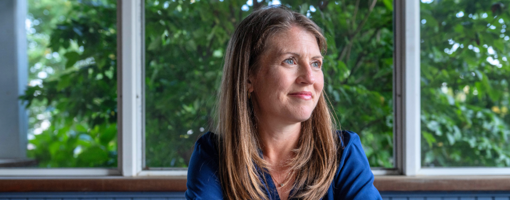 Amy Julia sits at a wooden table and looks off into the distance.