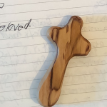lined paper in a notebook with hard-to-read writing and a wooden cross resting on top