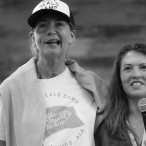 photo by Bryan Johnson of Amy Julia holding a mic and speaking as Katherine Wolf stands beside her and puts her arm around her