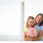photo of AJ holding young Penny on her lap outside with the ocean in the background