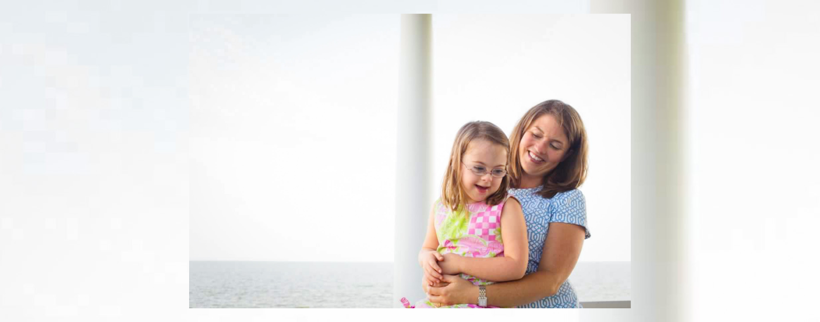 photo of AJ holding young Penny on her lap outside with the ocean in the background