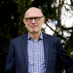 dark blue graphic with geometric shape overlays and the Reimagining the Good Life with Amy Julia Becker podcast logo in bottom right corner. In the middle of the graphic is a photo of Miroslav Volf, PhD