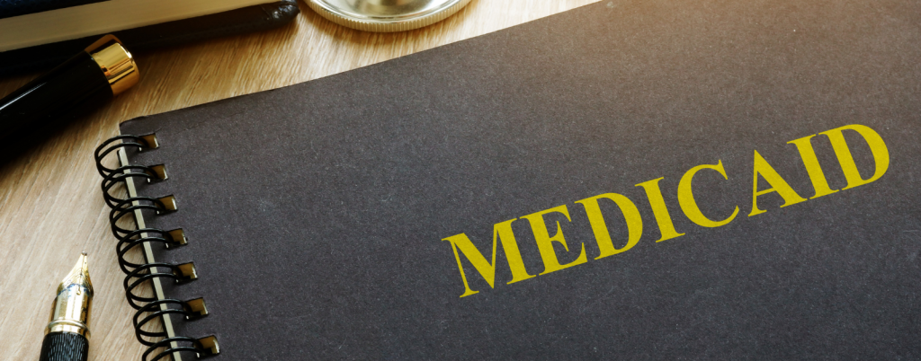 A stethoscope, glasses, and notebooks lie on a desk next to a folder labeled "Medicaid."
