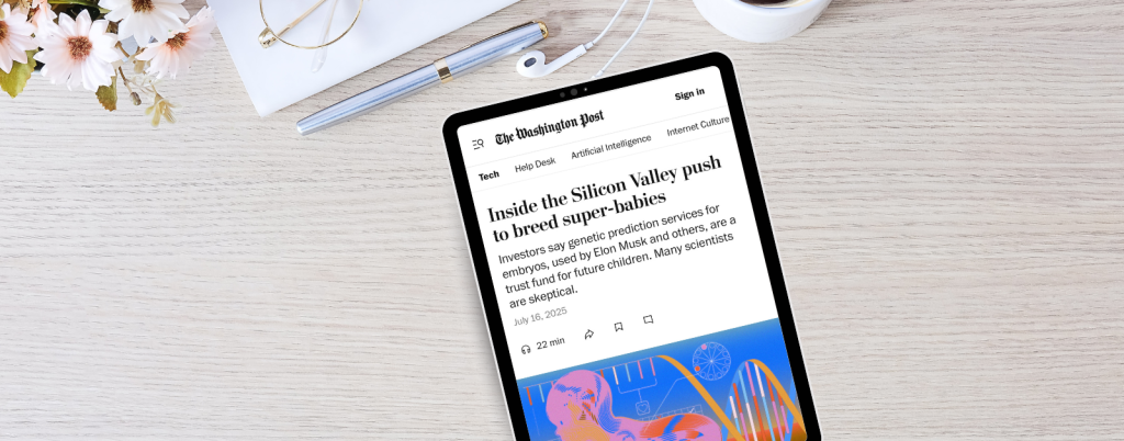 A tablet on a light wood desk displays a Washington Post article titled “Inside the Silicon Valley push to breed super-babies.” The subheading reads, “Investors say genetic prediction services for embryos, used by Elon Musk and others, are a trust fund for future children. Many scientists are skeptical.” The article is dated July 16, 2025, with an estimated 22-minute read time. The desk also features a pen, a white notebook, white earbuds, and a bunch of white and pink daisies in the corner.