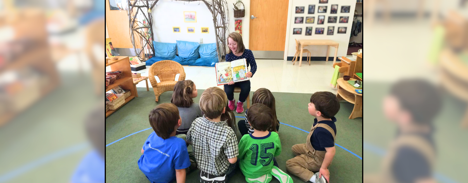 2015 photo of young Penny reading a book in a classroom to a group of children sitting in front of her