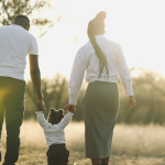 parents walking away from the camera holding the hands of their young child who toddles between them