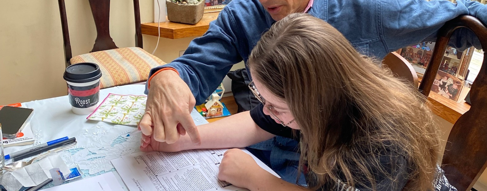 2023 photo of Peter sitting next to Penny. They are at a table covered with papers, pens, and a coffee cup. He’s pointing to a document as she is focused on reading it