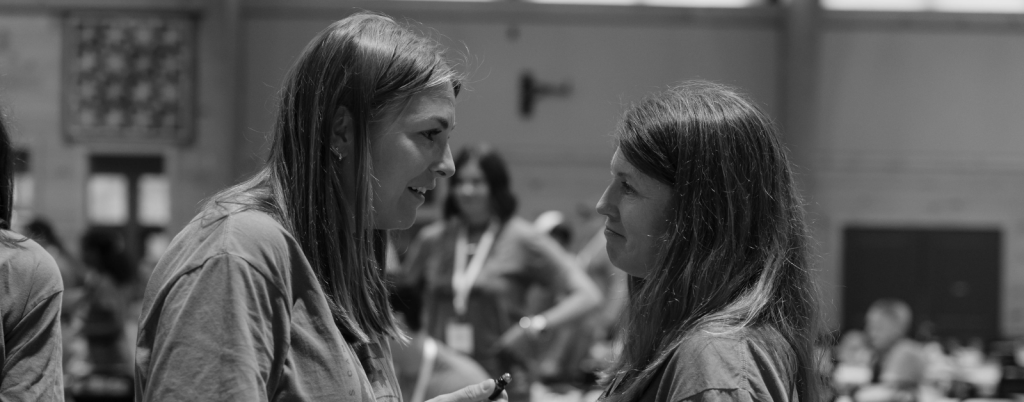 a friend and I face each other in deep conversation at Hope Heals Camp. The background shows a blurred group of people in a large indoor dining hall