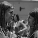 a friend and I face each other in deep conversation at Hope Heals Camp. The background shows a blurred group of people in a large indoor dining hall