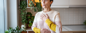 Joyful calm mature woman meditating with deep breathing, hands rest on chest. Breathing for relax
