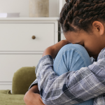 side profile of a child who is sad hiding her face in her knees