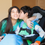 brother sitting in a wheelchair gives his sister a kiss on her cheek