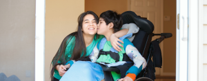 brother sitting in a wheelchair gives his sister a kiss on her cheek