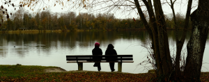 2 people sitting on a bench near a pond