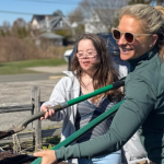Penny and her aunt work together outdoors, shoveling soil out of the back of a truck on a sunny day.