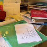 my desk overflowing with papers and stacks of books