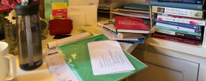 my desk overflowing with papers and stacks of books
