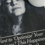 A white mug of black coffee sits on a wooden table beside a printed New York Times article. The article features a black-and-white portrait and the headline, “Want to ‘Optimize’ Your Happiness? This Happiness Expert Says: Don’t.”