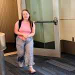 Penny, our daughter who has Down syndrome, walks out of a jet bridge after getting off a plane while a uniformed airline staff member stands nearby.