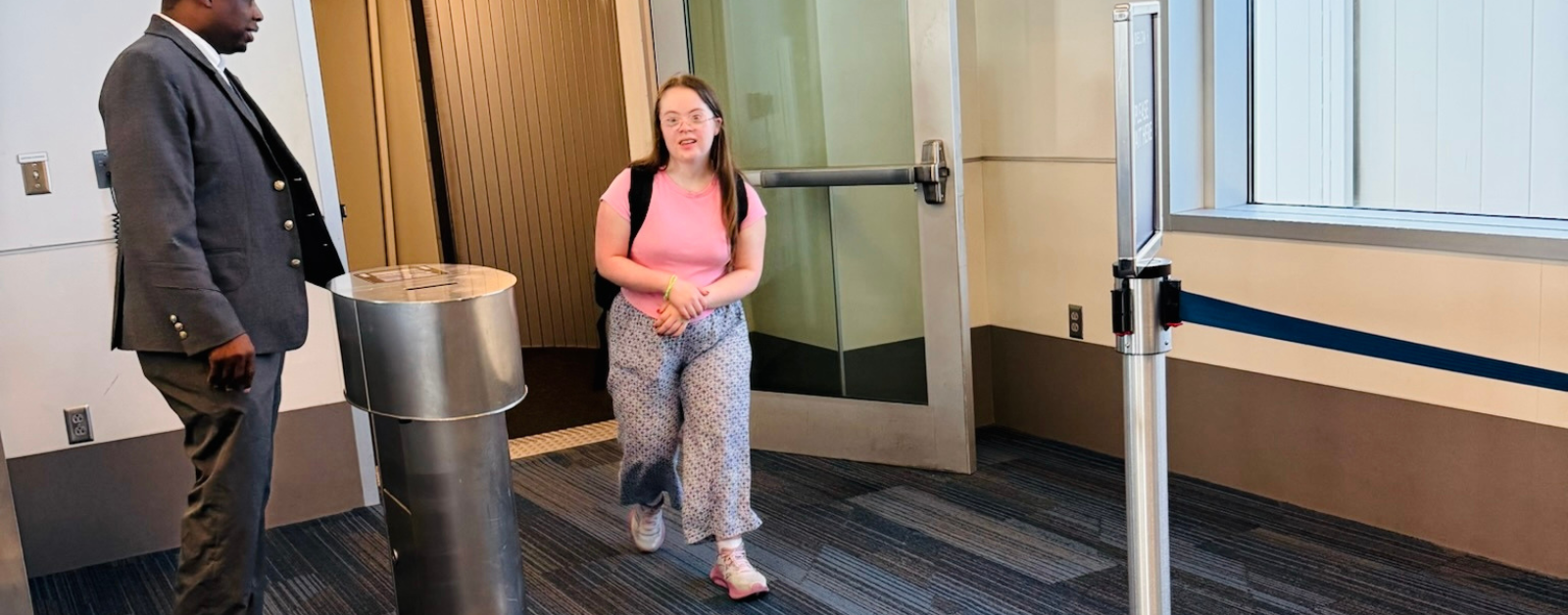 Penny, our daughter who has Down syndrome, walks out of a jet bridge after getting off a plane while a uniformed airline staff member stands nearby.