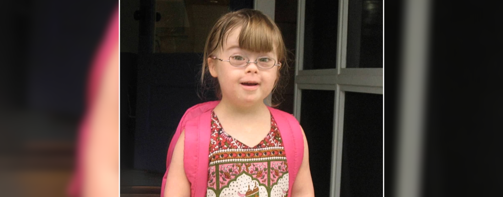 a 2010 photo of Penny wearing glasses and a pink backpack. She is smiling at the camera, dressed in a colorful patterned top