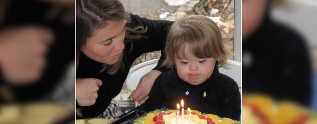 toddler Penny blows out candles on her birthday cake while Amy Julia leans in close