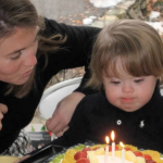 toddler Penny blows out candles on her birthday cake while Amy Julia leans in close