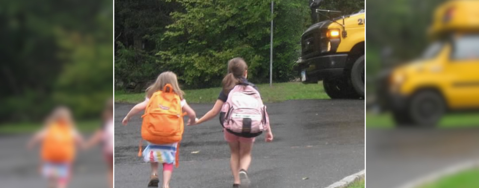 Penny and a friend wear backpacks and walk hand in hand across the street to a waiting yellow school bus