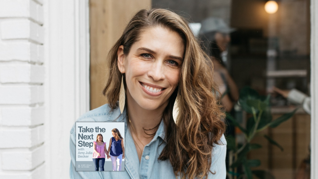 Monica DiCristina sits on a wooden bench outside a shop, wearing a light blue button-down shirt and black pants. She holds a white takeaway coffee cup and looks toward the camera. In the bottom middle is a small image of the podcast logo where Penny and Amy Julia walk hand in hand, with Amy Julia looking toward Penny.