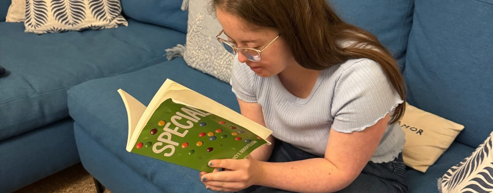 Penny sits on a blue couch reading the book Special. The book is partially visible in her hands, featuring a green cover with colorful candy-like dots and the title “SPECIAL” in large white letters.