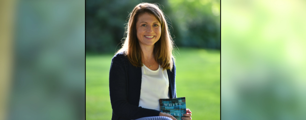 2018 photo of me sitting outside holding my book White Picket Fences