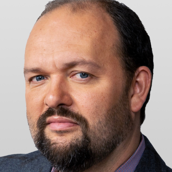 AJB-featured season 8 ross Douthat dark blue graphic with geometric shape overlays and the Reimagining the Good Life with Amy Julia Becker podcast logo in bottom right corner. In the middle of the graphic is a photo of Ross Douthat