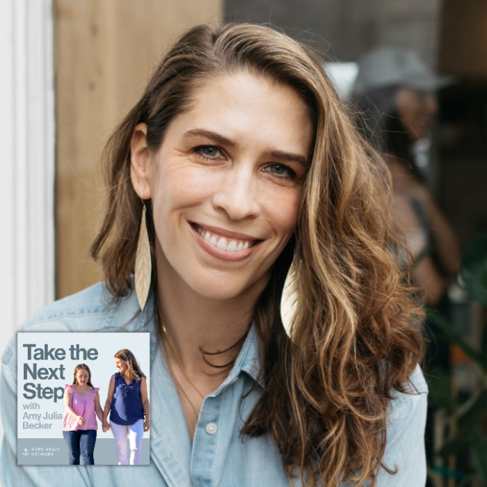 Monica DiCristina sits on a wooden bench outside a shop, wearing a light blue button-down shirt and black pants. She holds a white takeaway coffee cup and looks toward the camera. In the bottom middle is a small image of the podcast logo where Penny and Amy Julia walk hand in hand, with Amy Julia looking toward Penny.